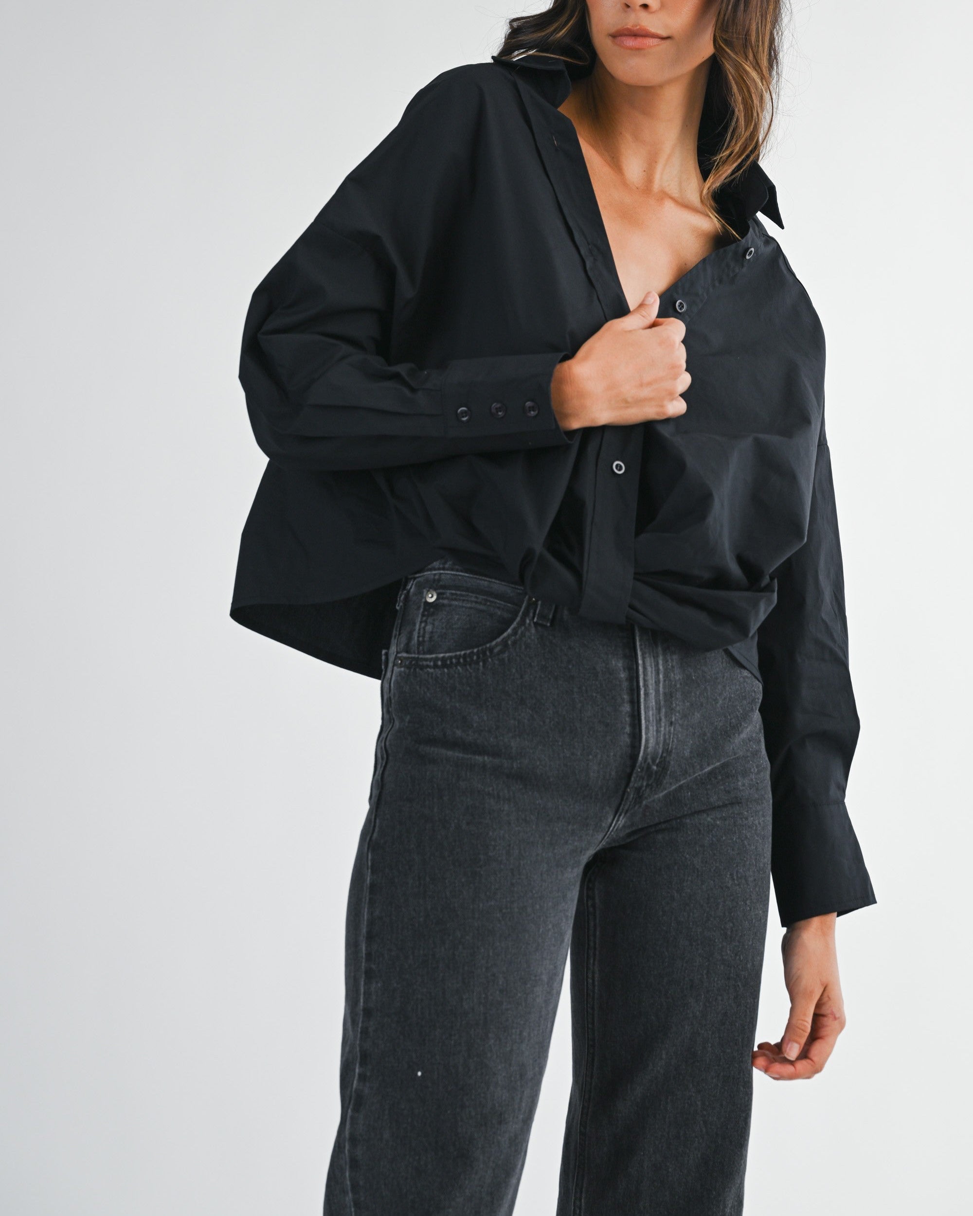 Woman wearing a black oversized shirt and dark jeans on a white background